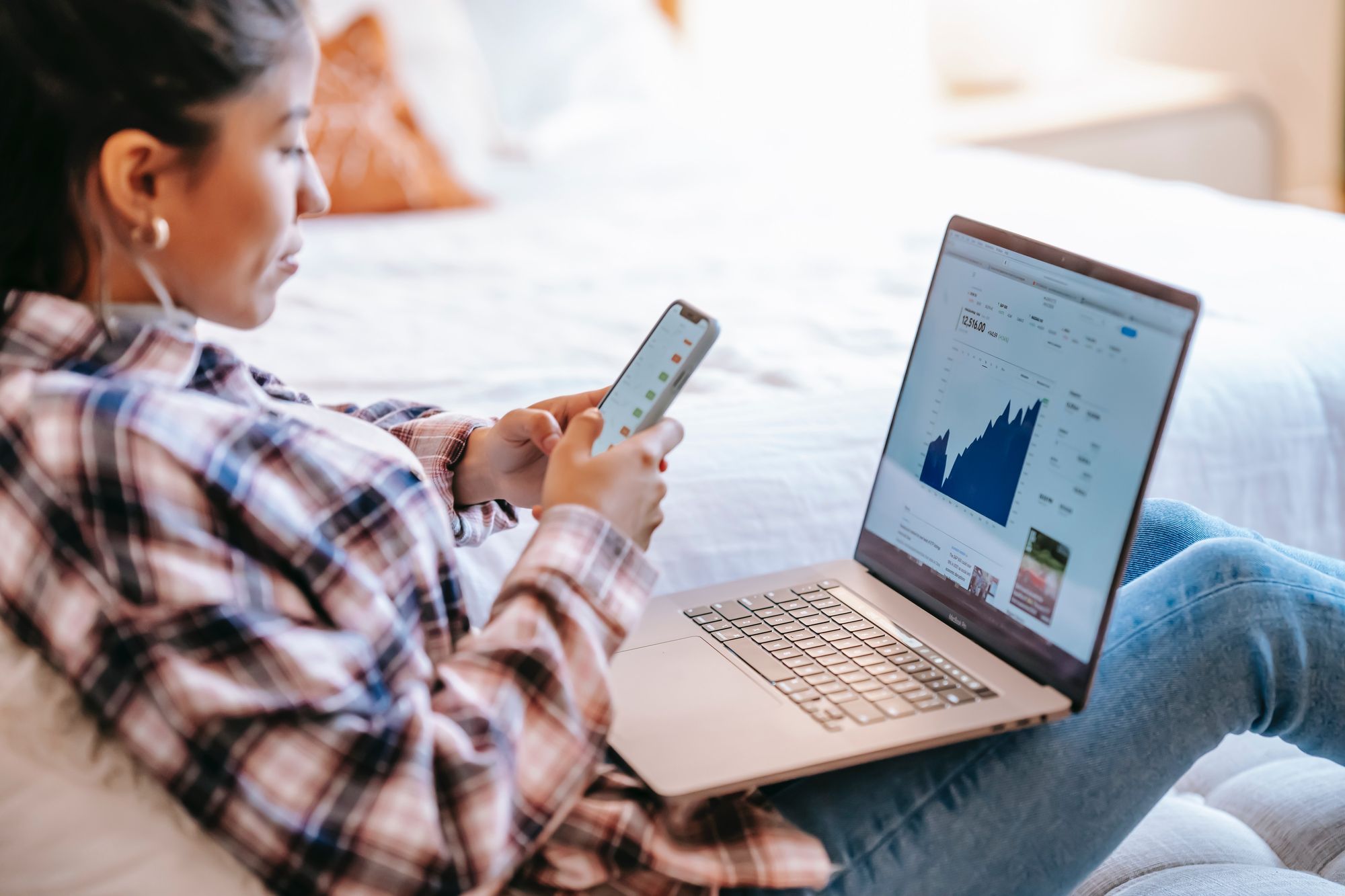 A woman using a phone and laptop to trade