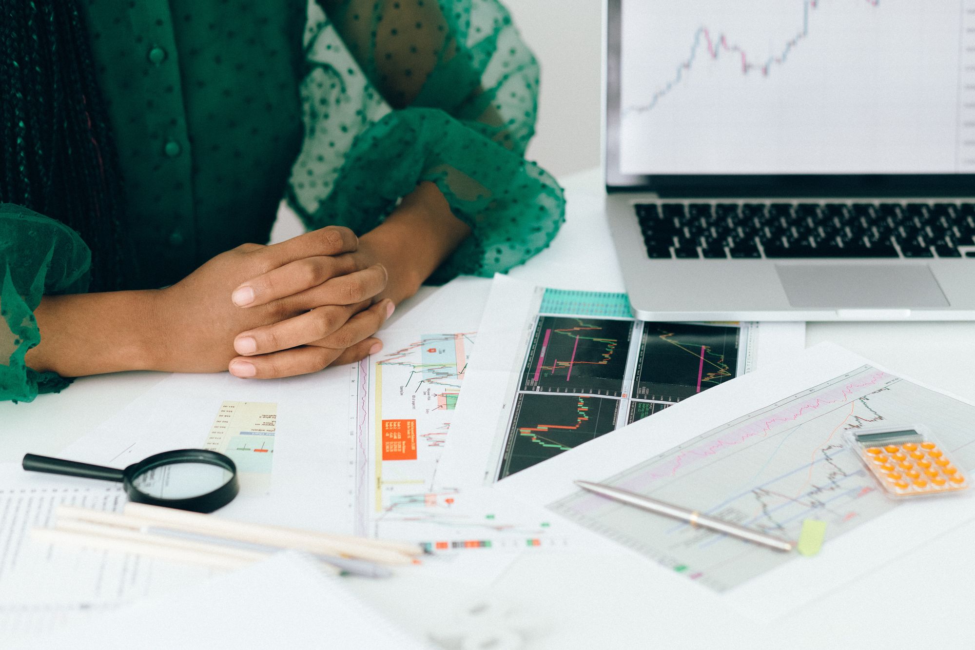 A woman sitting with her hands folded on a table with charts, a laptop and a calculator