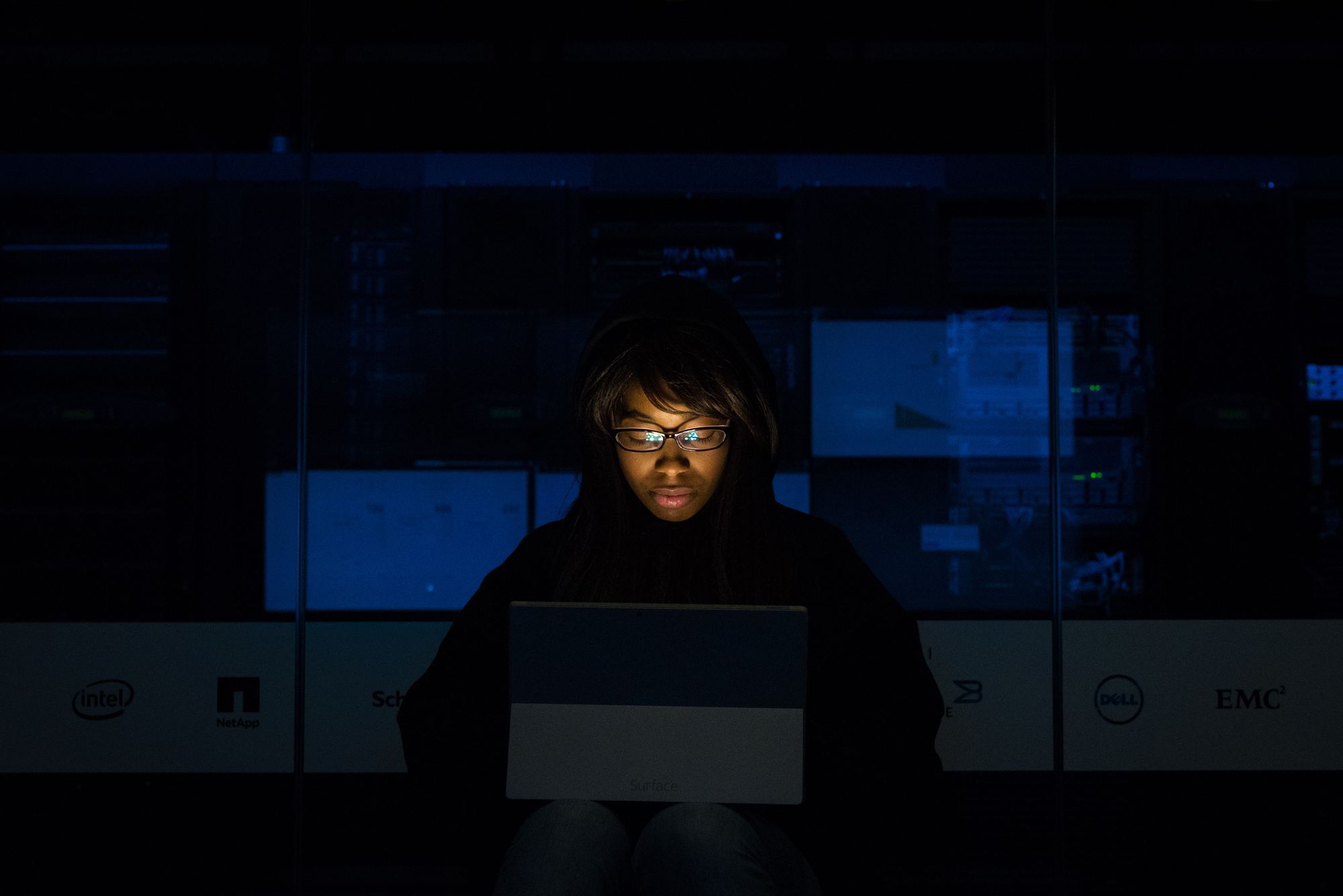 A woman wearing glasses and looking at a laptop in a darkly lit room